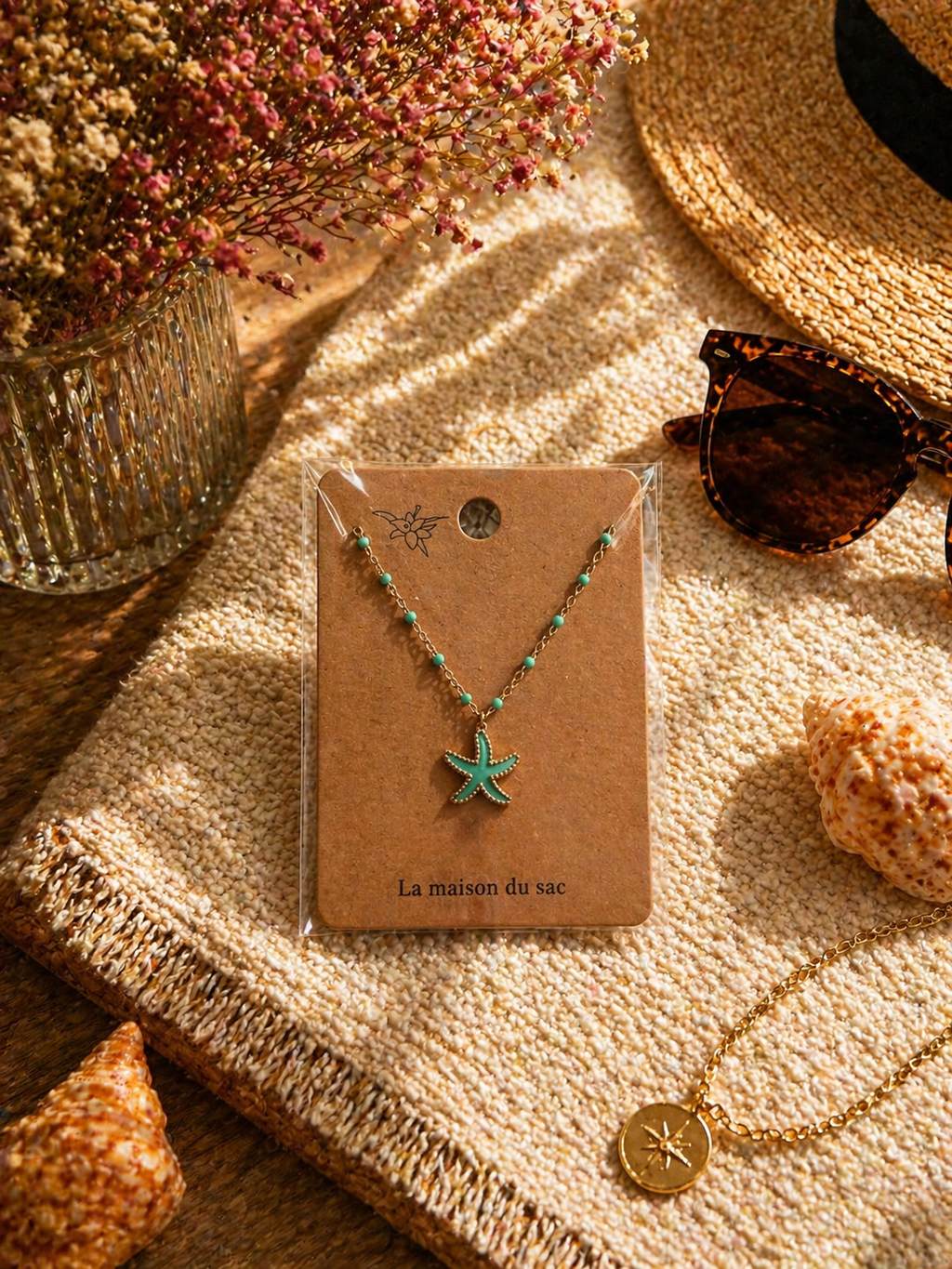Colliers dorés avec pendentif étoile de mer colorée, présentés sur cartes La Maison du Sac dans une ambiance estivale méditerranéenne avec coquillages, chapeau de paille et lunettes de soleil.
