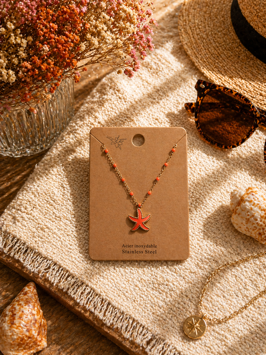 Colliers dorés avec pendentif étoile de mer colorée, présentés sur cartes La Maison du Sac dans une ambiance estivale méditerranéenne avec coquillages, chapeau de paille et lunettes de soleil.