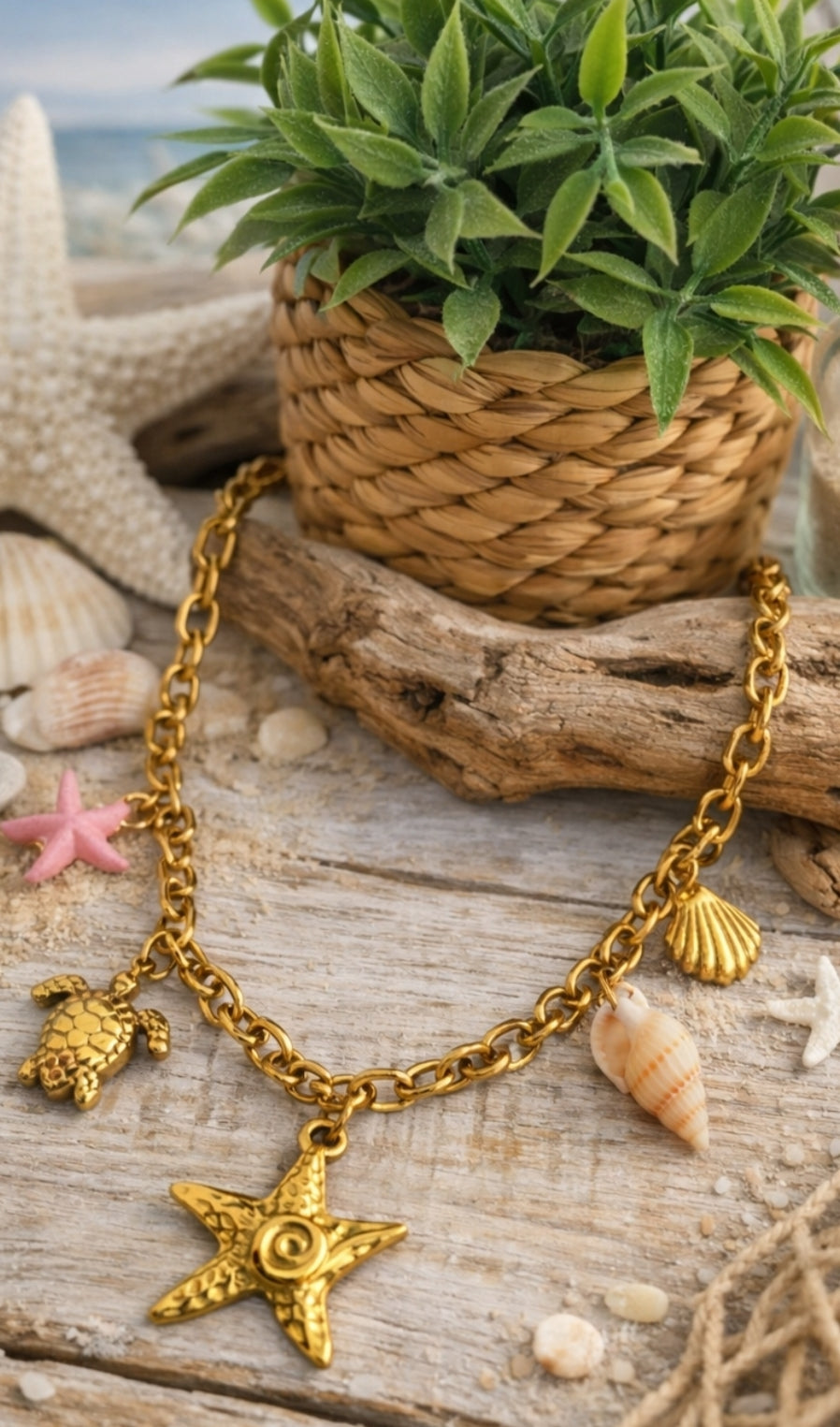 Collier Procida en acier inoxydable doré avec charms marins, étoile de mer, tortue, coquillages et détail rose sur décor plage.