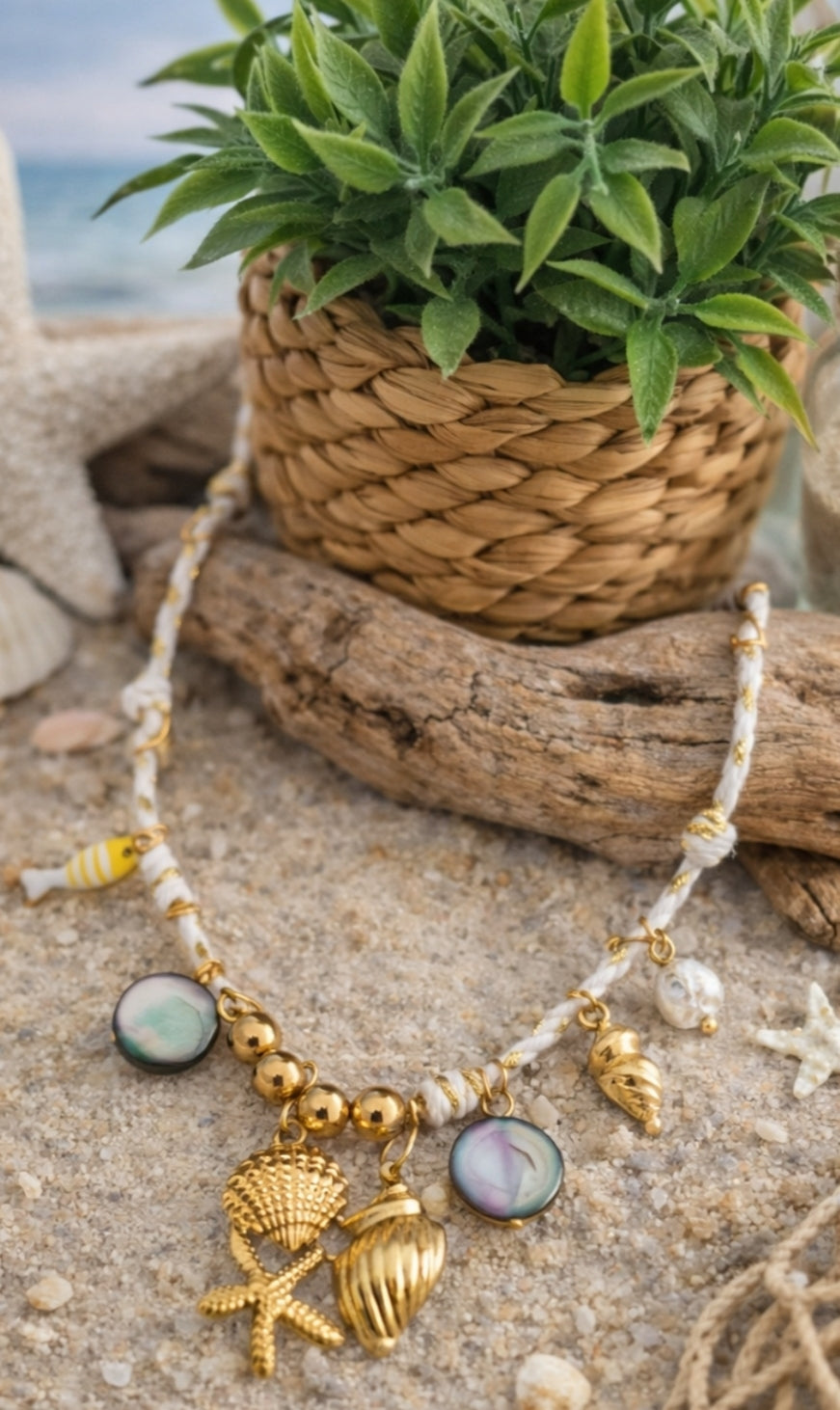 Collier Ischia en acier inoxydable doré avec cordon blanc, charms coquillages, étoile de mer, perles, poisson et détails nacrés sur décor plage.