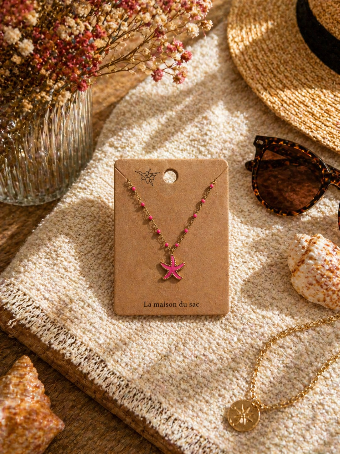 Colliers dorés avec pendentif étoile de mer colorée, présentés sur cartes La Maison du Sac dans une ambiance estivale méditerranéenne avec coquillages, chapeau de paille et lunettes de soleil.