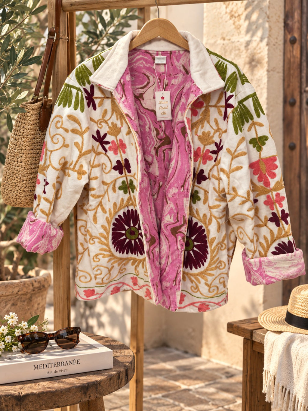 Veste brodée en velours camel mise en scène sur cintre dans une ambiance méditerranéenne